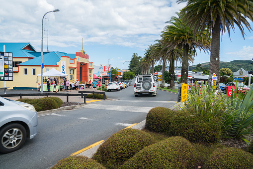 View along Bow Street in small town on busy summer Sunday morning vehicles, local market and people moving about in busy holiday town of Raglan New Zealand.