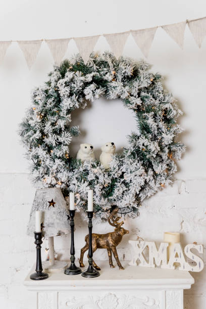 A traditional bright Christmas wreath hanging over the fireplace, on a white brick wall, home decor for winter holidays,fireplace with candles. Christmas concept, new year.Greetings card. A traditional bright Christmas wreath hanging over the fireplace, on a white brick wall, home decor for winter holidays,fireplace with candles. Christmas concept, new year.Greetings card. advent candle wreath christmas stock pictures, royalty-free photos & images