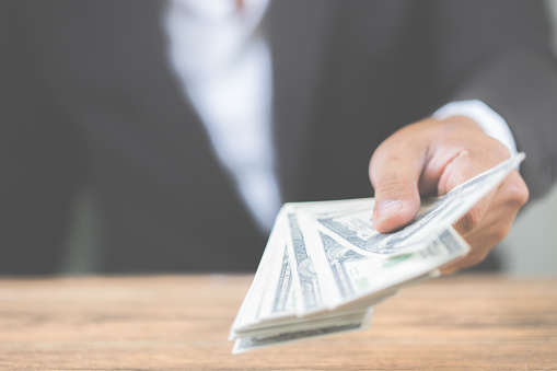 Close up hand of businessman holding money dollar bills on wooden table. Using as concept of corruption , Business corruption, bribe. With copy space for your text.