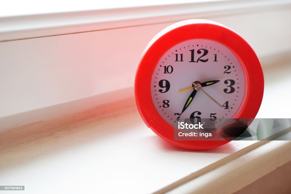 Orange frame round shape alarm clock Orange frame round shape alarm clock with white dial on wooden window sill with copy space for text. Black Color Stock Photo