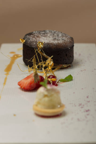 istock Luxurious dessert with brownie,  vanilla ice-cream placed on a macaron,  strawberries,  mint,  decorated with gold leafs and caramelized sugar – on a white plate,  brown background 1077512790