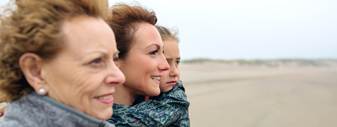 Closeup of three generations female looking at sea on the beach in autumn. Background focus on young woman and child