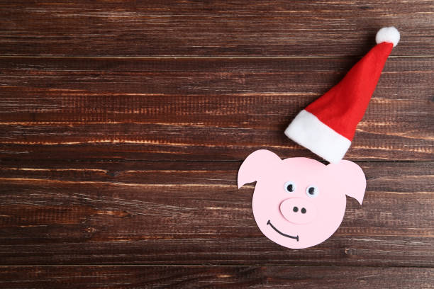 Paper pig with santa hat on brown wooden table