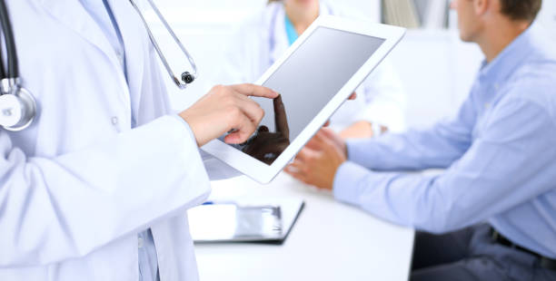 istock Doctor using tablet computer, close-up of hands at touch pad screen. Patient is at the background. 1077528242