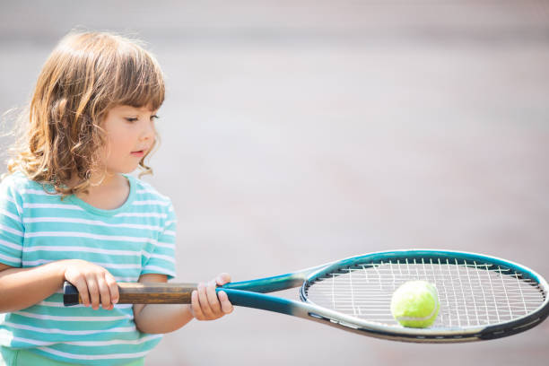 niño aprendiendo a jugar al tenis en la cancha al aire libre. niña con raqueta de tenis. - tennis child childhood sport fotografías e imágenes de stock