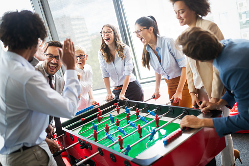 Business people having great time together. Colleagues playing table football in office
