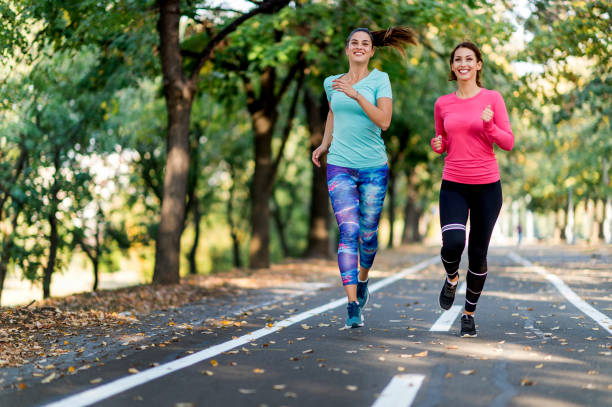 istock Two female friends jogging on path in sunny park 1077548124