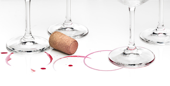 Rest of wine, cork and empty wine glasses against white background.\nRemains of end of party