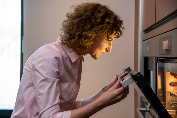 side view of woman checking food in the oven - oven imagens e fotografias de stock