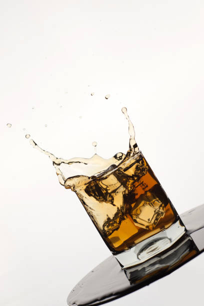 istock Tilted Glass of splashing whiskey with ice isolated on white 1077551682