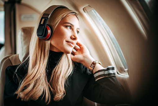 Young successful blonde woman sitting on a private jet and listening to music through headphones.