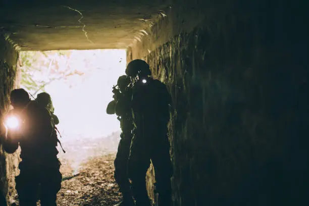 Group of soldiers in camouflaged clothing on a mission in dark cave.