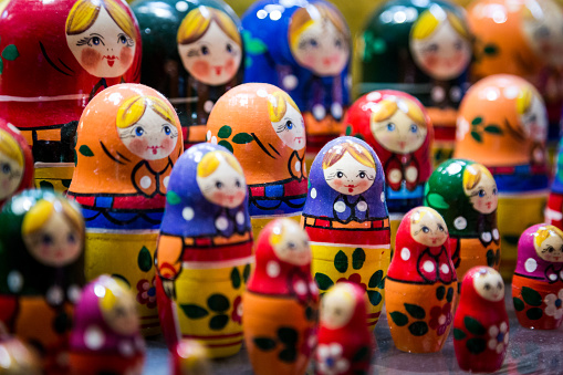 Close up color image depicting a large collection of wooden Russian nesting dolls in a row and for sale on a shop shelf. Selective focus on some of the wooden dolls, while others are defocused in the background. Room for copy space.