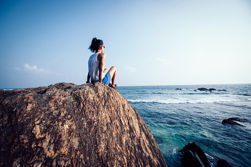Young woman sit on seaside rock cliff edge looking at the distance