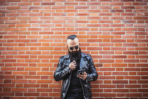 Biker with with beard and leather jacket texting on the street
