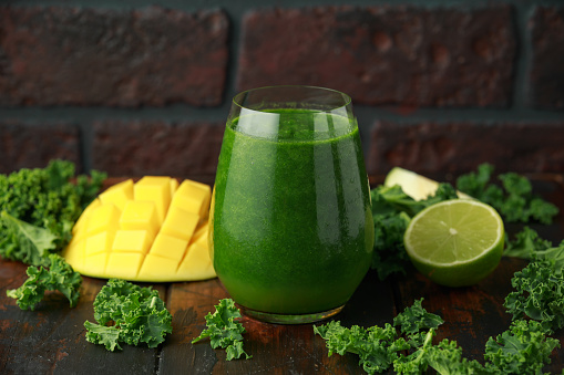 Green smoothies with kale and mango on wooden table.