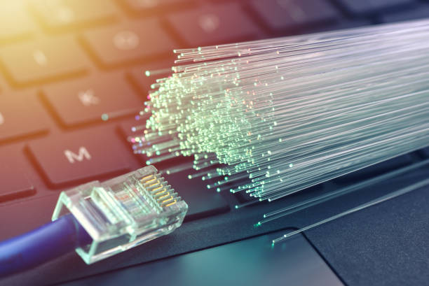 istock Fiber optics in blue, close up with ethernet and keyboard background, warm lens flare 1077605272