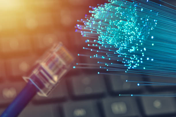 istock Fiber optics in blue, close up with ethernet and keyboard background, warm lens flare 1077605342