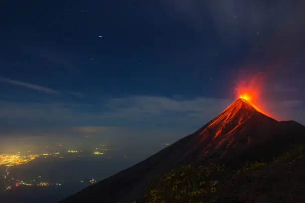 Volcan de Fuego in Guatemala erupts at night time over the city lights of Southern Guatemala
