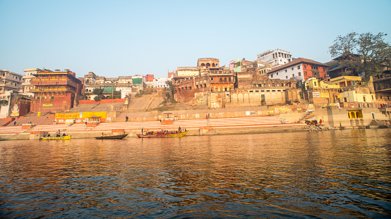 Historic Varanasi city with ancient temples and buildings along the Ganges river ghat as viewed from a boat at sunrise.