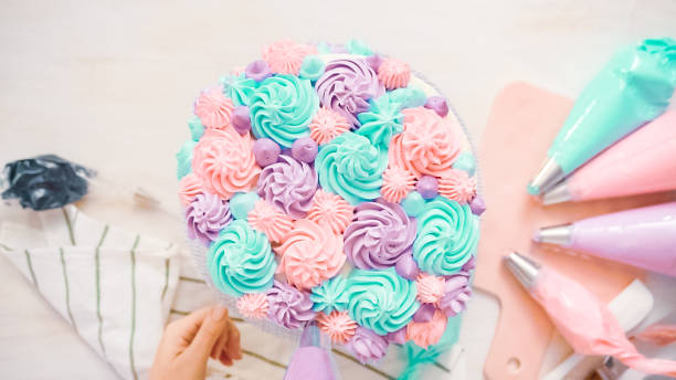 Flat lay. Piping pastel color buttercream rosettes on a white cake to make a unicorn cake.