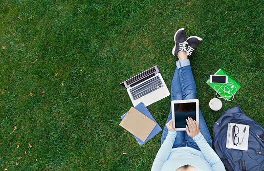 Top view of girl sitting in park with laptop, tablet, smartphone, backpack and coffee. Copy space on screens