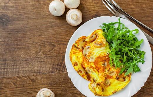 Omelet with mushrooms and arugula salad in white plate on wooden table background.