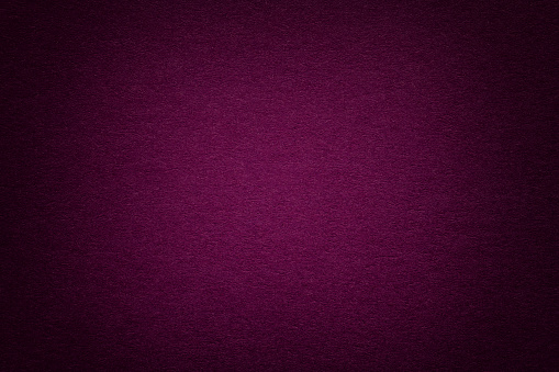 Texture of vintage dark purple paper background with vignette. Structure of dense magenta kraft cardboard with frame. Felt wine gradient backdrop closeup.