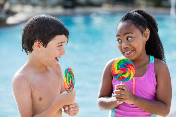istock Two multi-ethnic children sitting by pool with lollipops 1077648160