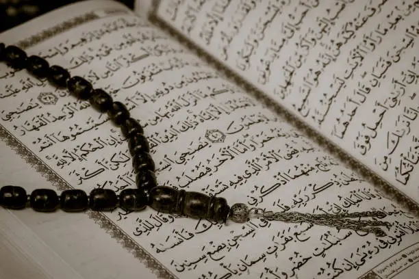Image portrays Tasbeeh prayer beads against the backdrop of Quranic script.