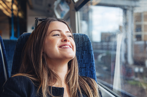 Smiling young woman traveling by train and watching outside in London