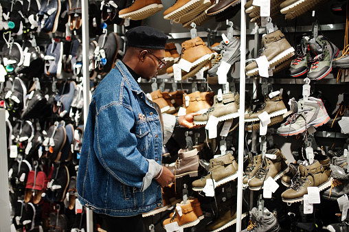 Stylish casual african american man at jeans jacket and black beret at clothes store trying new footwear.