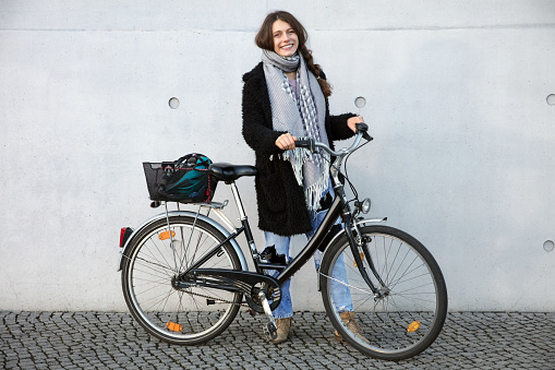 Full length portrait of beautiful young woman with her bicycle. Smiling caucasian female with her cycle standing outdoors in the city.