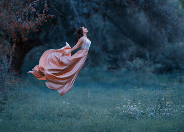 A young woman, a mysterious witch is floating in the air like a butterfly. A luxurious, long dress waving in the wind. Cold forest background. Enchanted princess. Art photo of levitation A young woman, a mysterious witch is floating in the air like a butterfly. A luxurious, long dress waving in the wind. Cold forest background. Enchanted princess. Art photo of levitation. female magician stock pictures, royalty-free photos & images