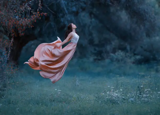 Photo of A young woman, a mysterious witch is floating in the air like a butterfly. A luxurious, long dress waving in the wind. Cold forest background. Enchanted princess. Art photo of levitation