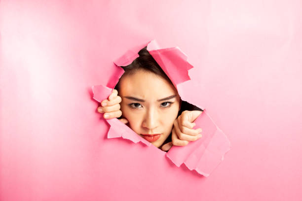 istock Asian woman expression through torn paper hole 1077673950