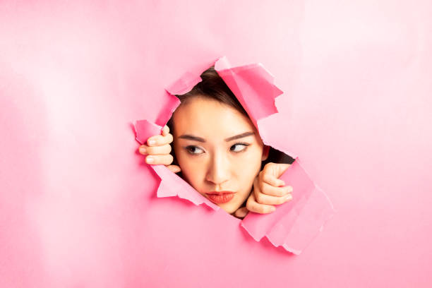 istock Asian woman expression through torn paper hole 1077674560