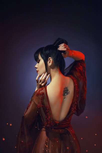 日本のゴージャスなセクシーな柔らかい黒髪姫、深いネックラインと蓮光赤いドレスの若い侍の女性は、彼女の背中にタトゥーします。青色の背景色とオレンジ色の炎火のアート写真 - tattoo lotus japanese culture women ストックフォトと画像