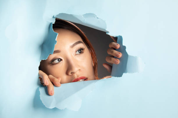 istock Asian woman expression through torn paper hole 1077678594