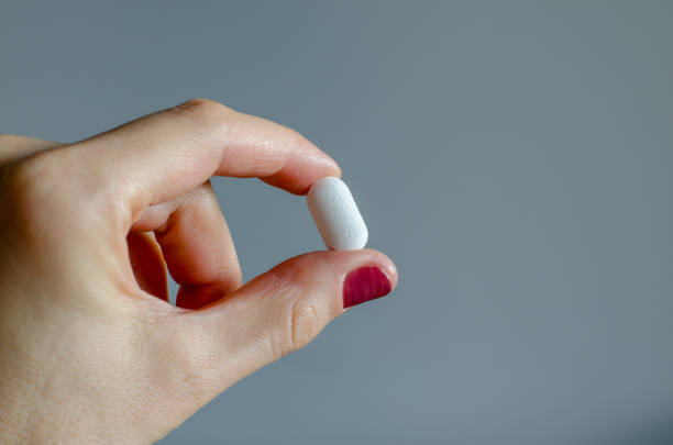 istock White pill in woman's hand on blue background 1077680524