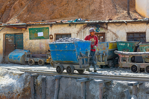 A bolivian miner with a carriage filled with rocks containing silver by a mine shaft of the Cerro Rico in the city of Potosi, Bolivia.