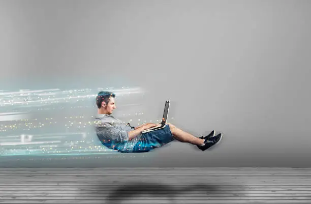 Fast levitating man in a white room using a laptop. High speed browsing.