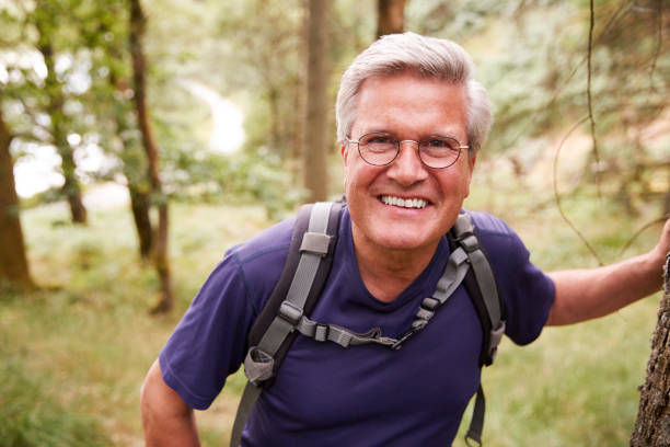 istock Middle aged Caucasian man taking a break leaning on a tree during a hike in a forest, smiling to camera, close up 1077689926