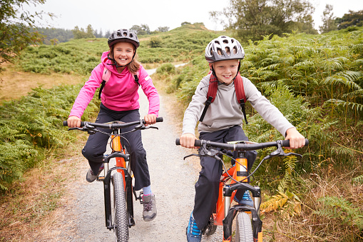 Two children riding mountain bikes on a country path laughing, front view