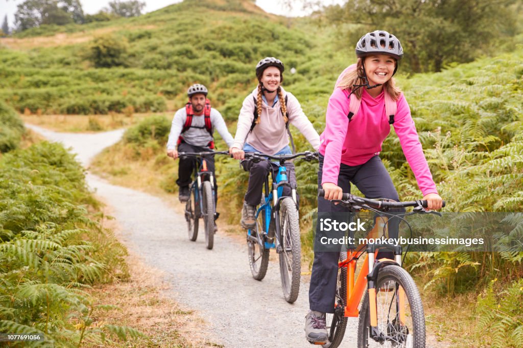Pre-teen girl riding mountain bike with her parents during a family camping trip, close up Cycling Stock Photo