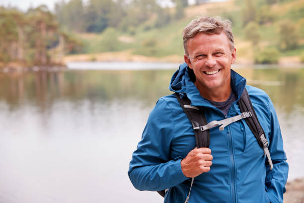 adult man on a camping holiday standing by a lake smiling to camera, close up, lake district, uk - backpack one mature man only only mature men one man only imagens e fotografias de stock
