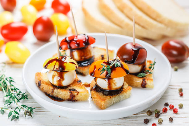 istock Bread toast with tomato cherry, mozzarella cheese, thyme and balsamic glaze on white wooden background. Canape. bruschetta. Gourmet snack. Selective focus 1077698156