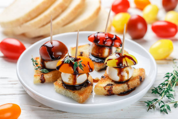 bread toast with tomato cherry, mozzarella cheese, thyme and balsamic glaze on white wooden background. canape. bruschetta. gourmet snack. selective focus - baguette vinegar balsamic vinegar glazed imagens e fotografias de stock