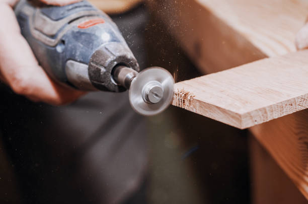 dremel 도구와 함께 설치 된 작은 원형 톱을 들고 남자의 손. 목재 처리입니다. 워크숍입니다. 나무 제품의 제조입니다. 결합의 절단 도구 - rotary international 뉴스 사진 이미지