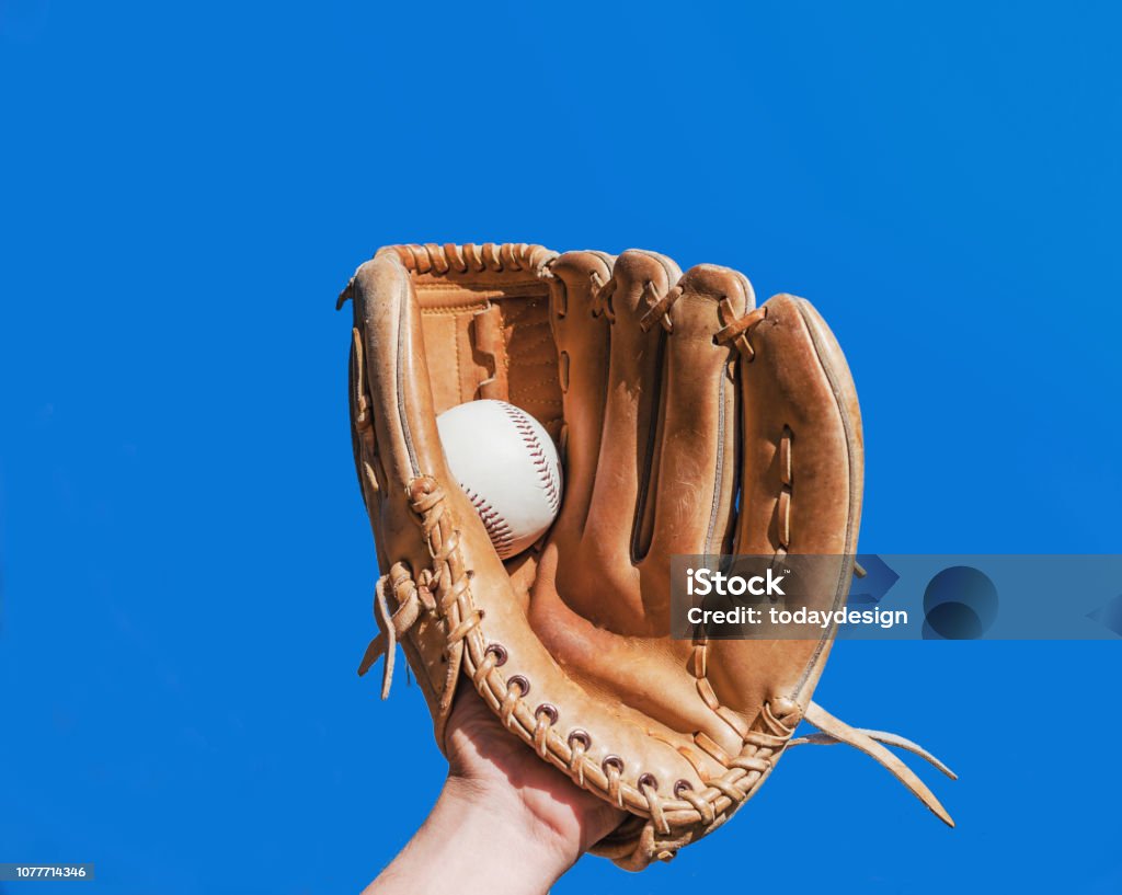 Hand in glove for a baseball game caught a leather white ball on a blue sky background. Sports contests. Victory. Achievement of success. Baseball Glove Stock Photo